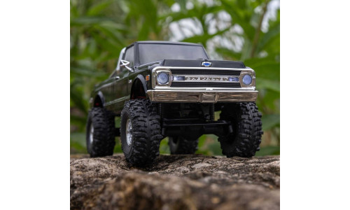 Axial SCX30 Chevrolet K10 RC truck climbing rocks outdoors, showcasing lifted suspension and chrome bumper